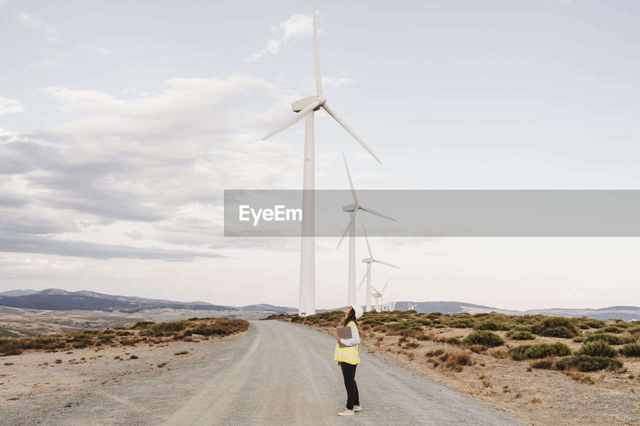 Engineer standing on dirt road by wind turbines at wind farm