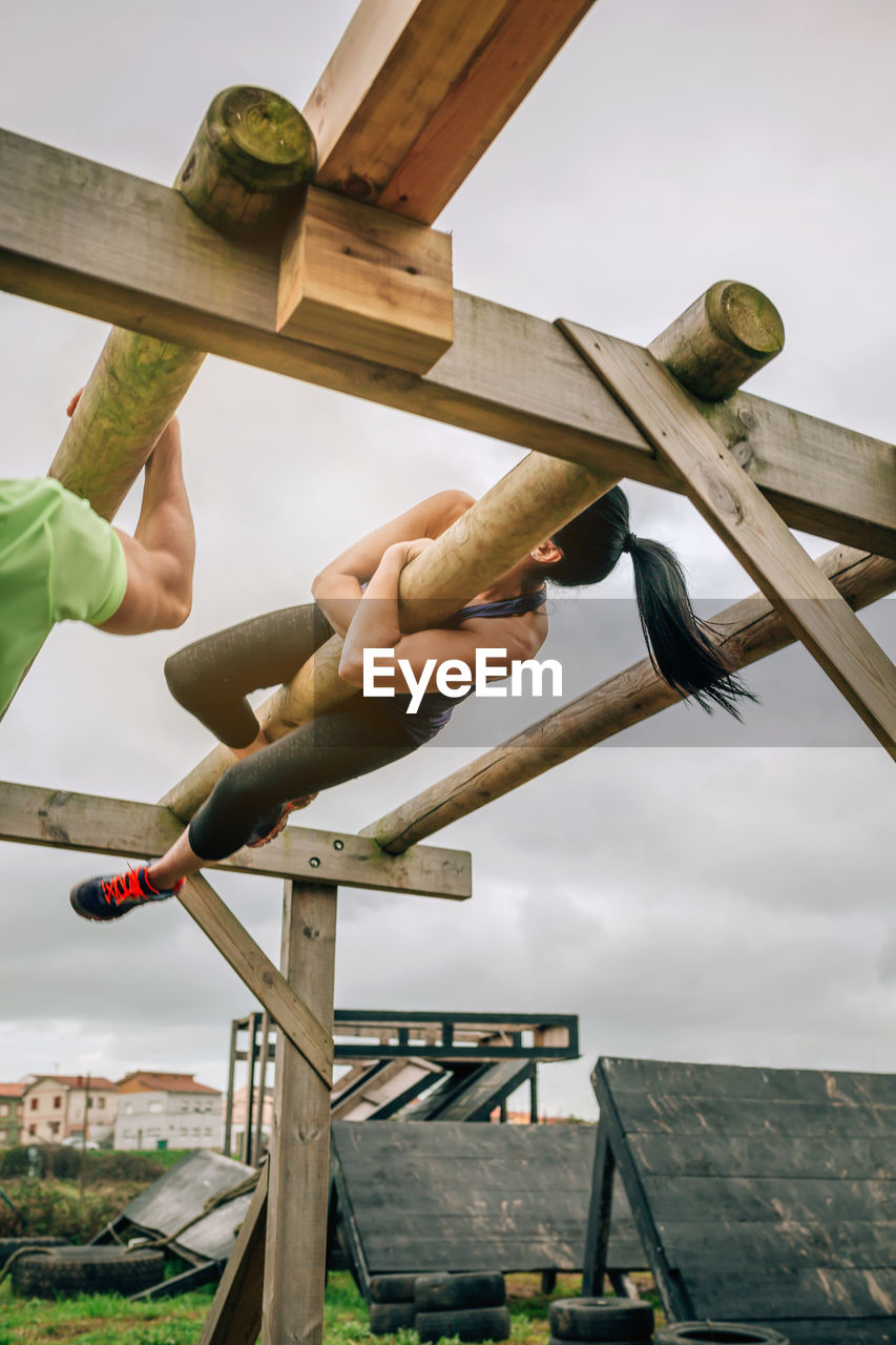 Low angle view of woman hanging on log against sky