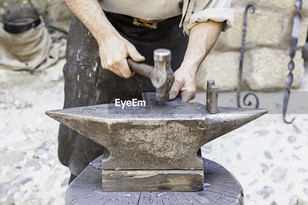 Midsection of man hammering metal at workshop