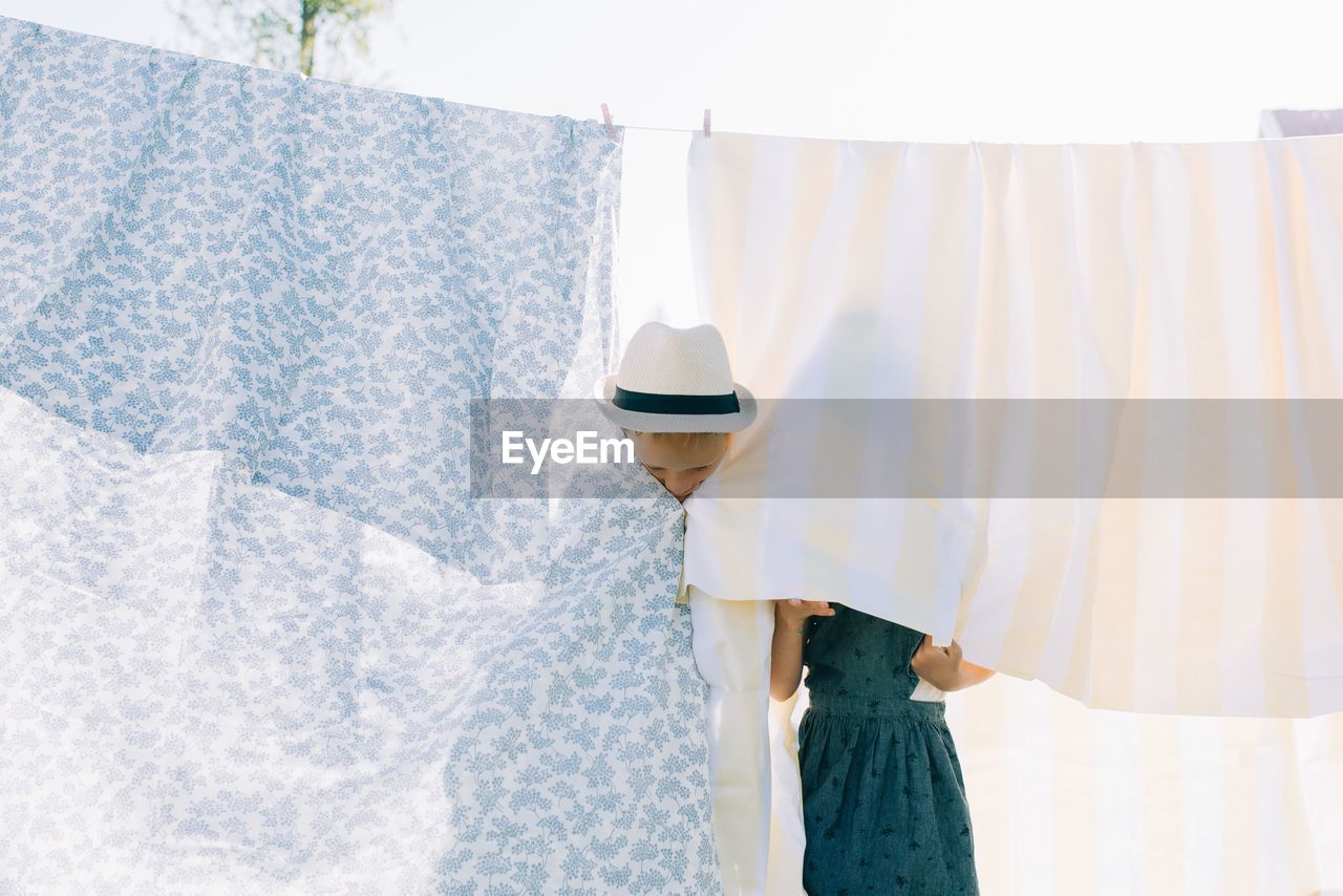 Siblings hiding behind the washing drying on the line at home