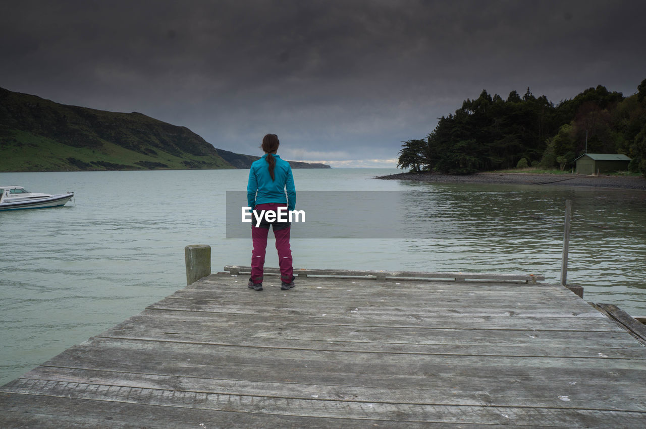 Rear view of woman standing on pier over sea against sky