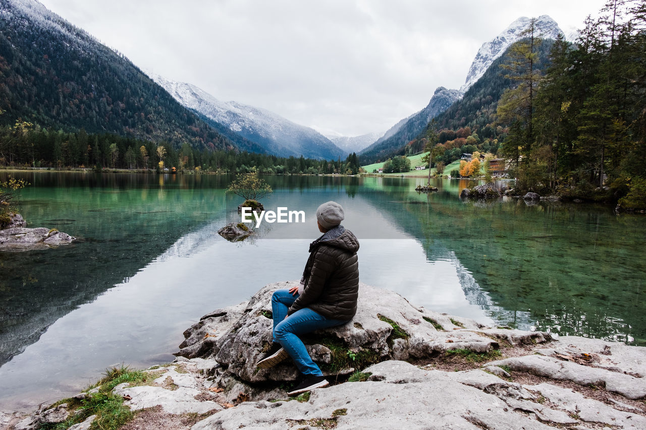 Full length of woman sitting on rock by lake against sky