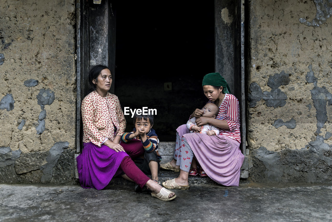 FULL LENGTH OF WOMEN SITTING ON WALL OF BUILDING