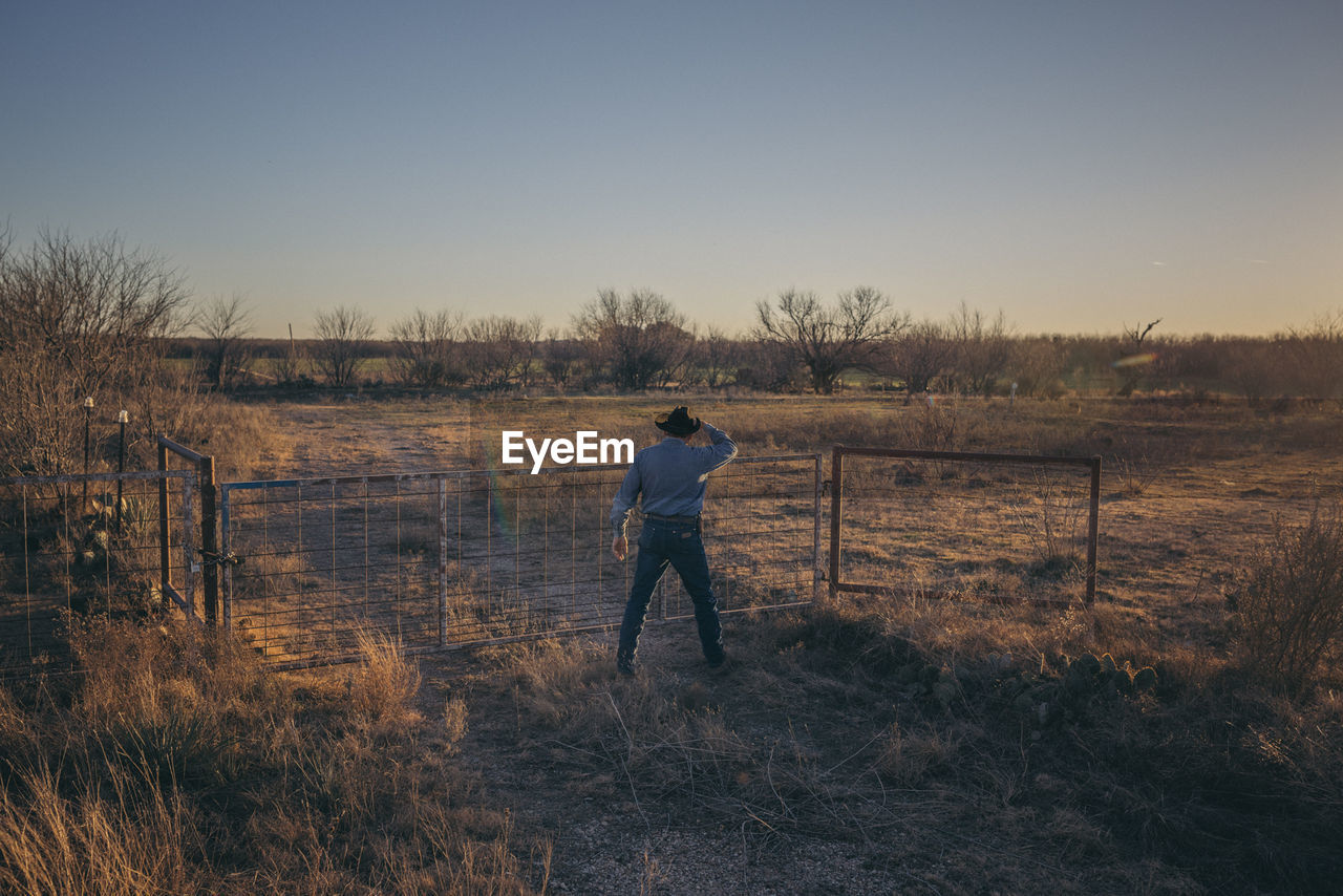 Rear view of man standing on field against clear sky