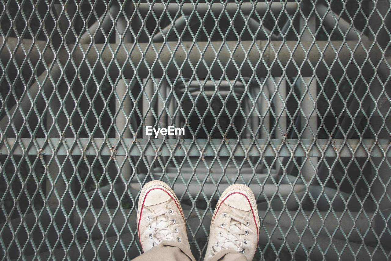 Low section of man standing on chainlink fence