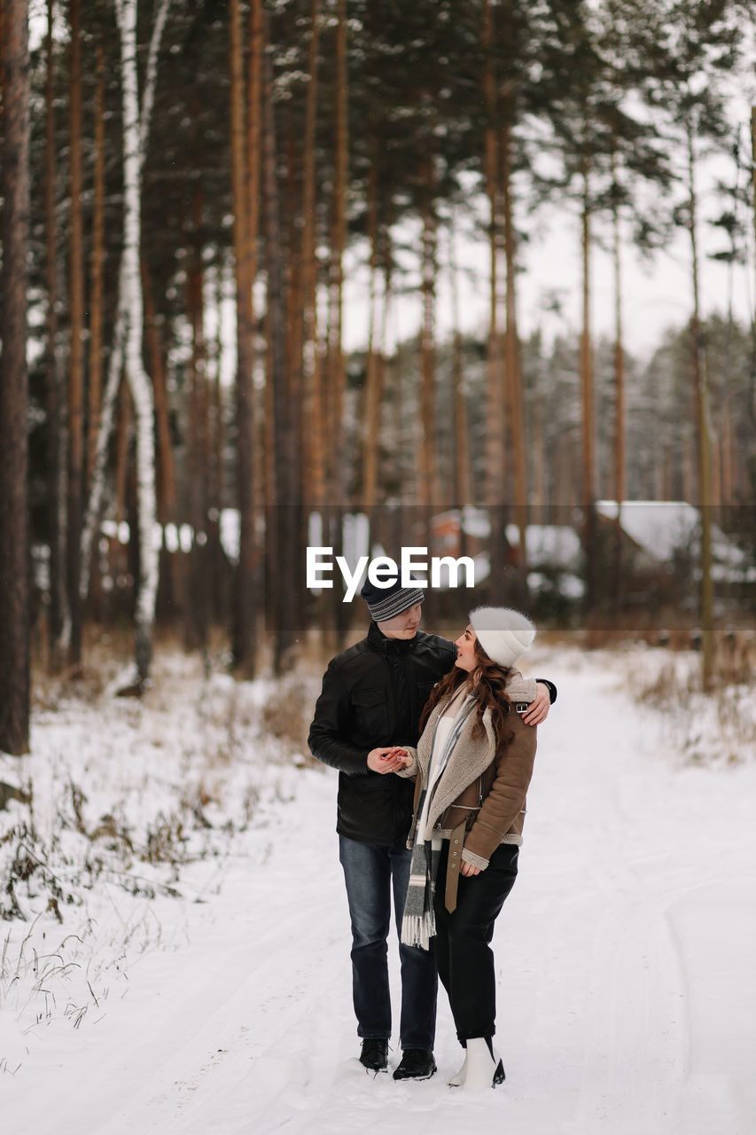 A happy couple in love in winter clothes hugging together walking in a snowy forest on an weekend