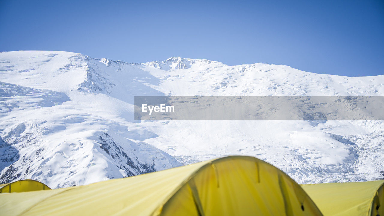 snow, mountain, cold temperature, winter, scenics - nature, mountain range, beauty in nature, environment, sky, adventure, landscape, nature, snowcapped mountain, blue, tent, travel destinations, tranquil scene, yellow, travel, camping, tranquility, day, no people, mountain peak, non-urban scene, clear sky, outdoors, vacation, trip, frozen, extreme terrain, holiday, glacier, ice, sports, tourism, sunny, remote, leisure activity, transportation, idyllic