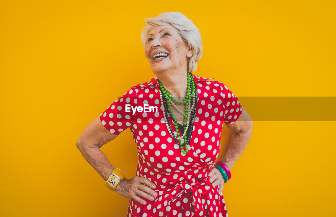 Smiling senior woman standing against yellow background