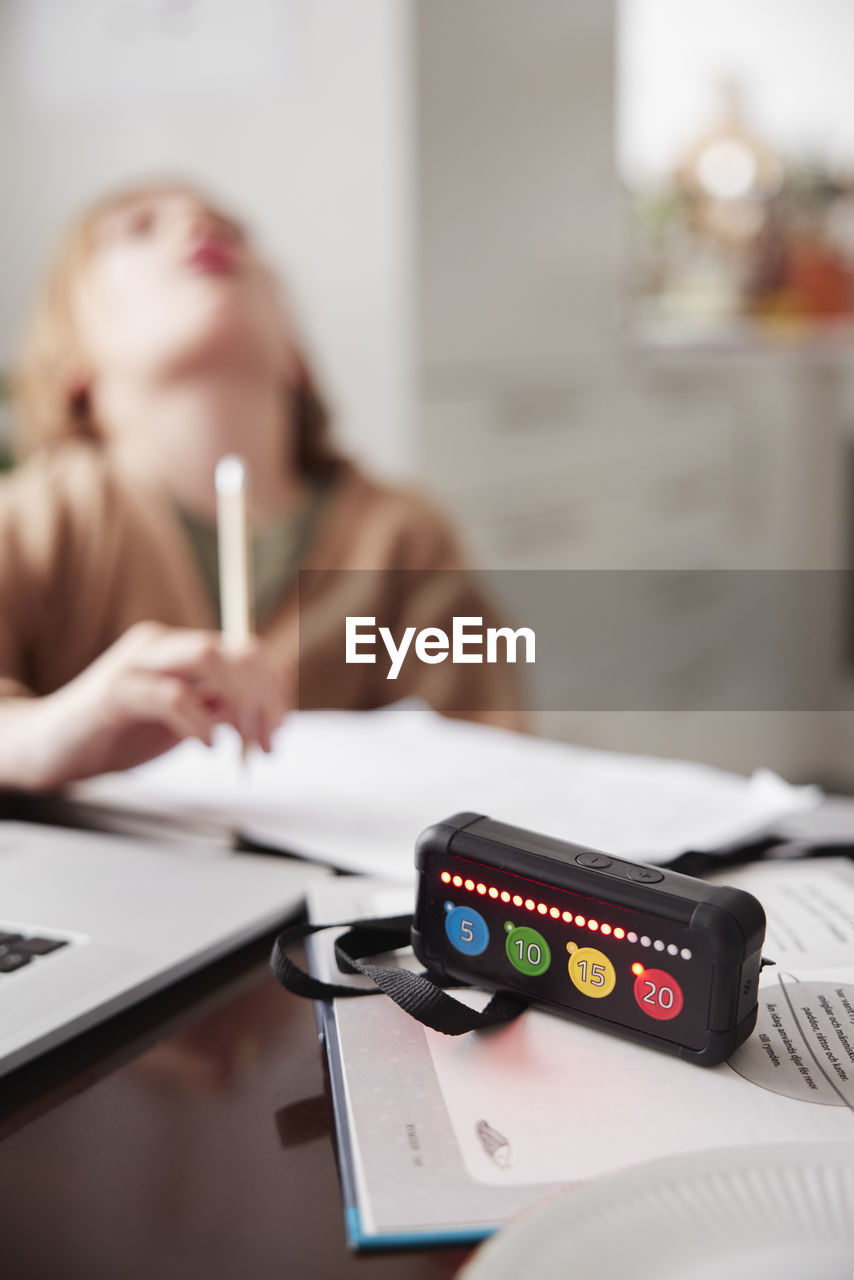 Electronic game on table, girl doing homework in background