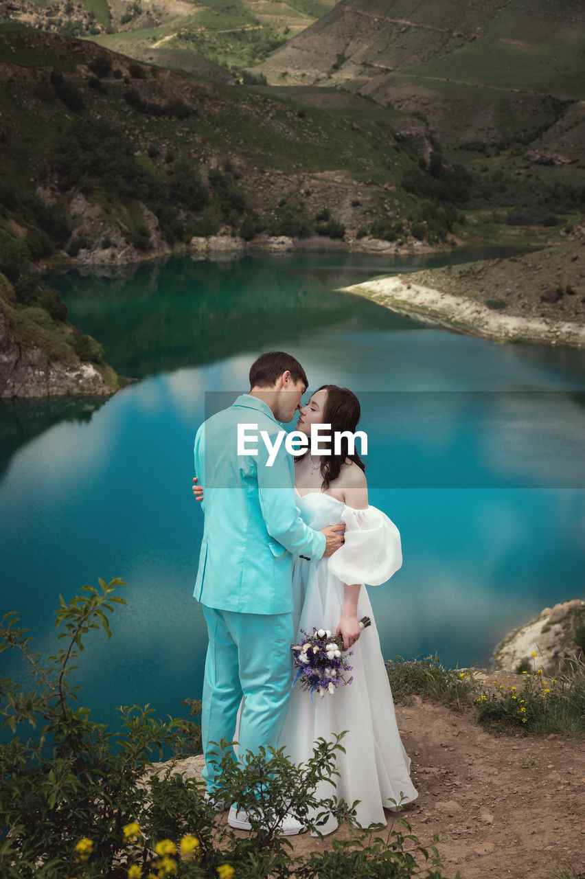 Beautiful wedding couple hugs tenderly against the backdrop of a mountain river and lake, the bride