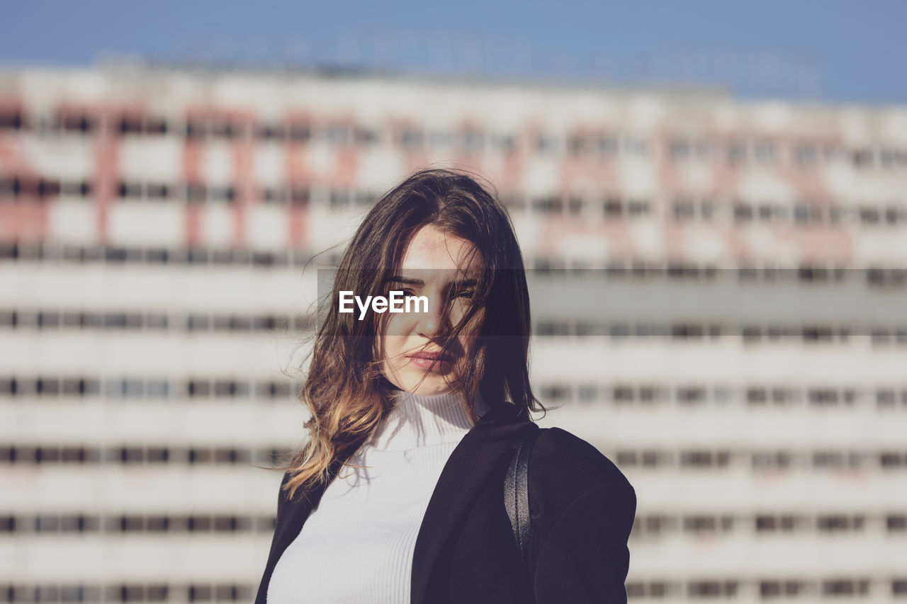 Portrait of young woman against building in city