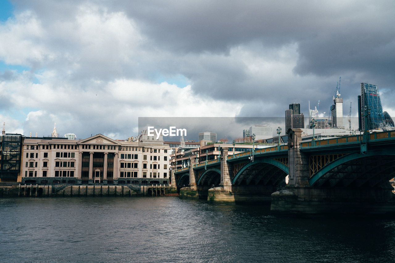 Bridge over river by buildings against sky in city