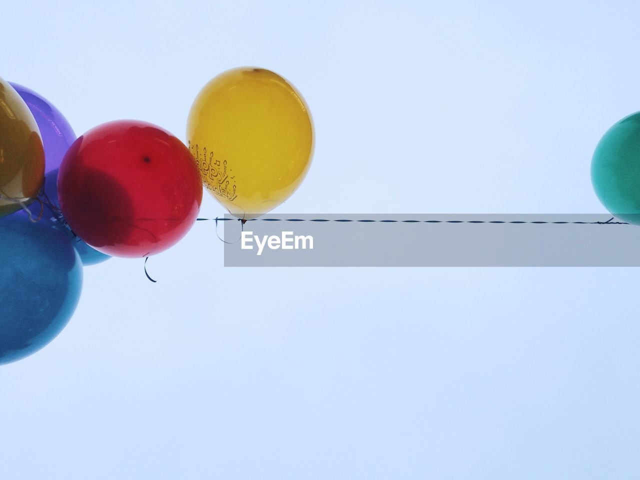 Low angle view of colorful balloons hanging from string against sky