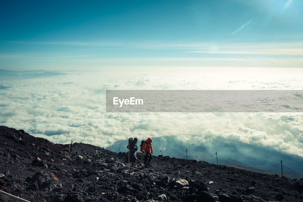 Hikers climbing mountain against cloudscape