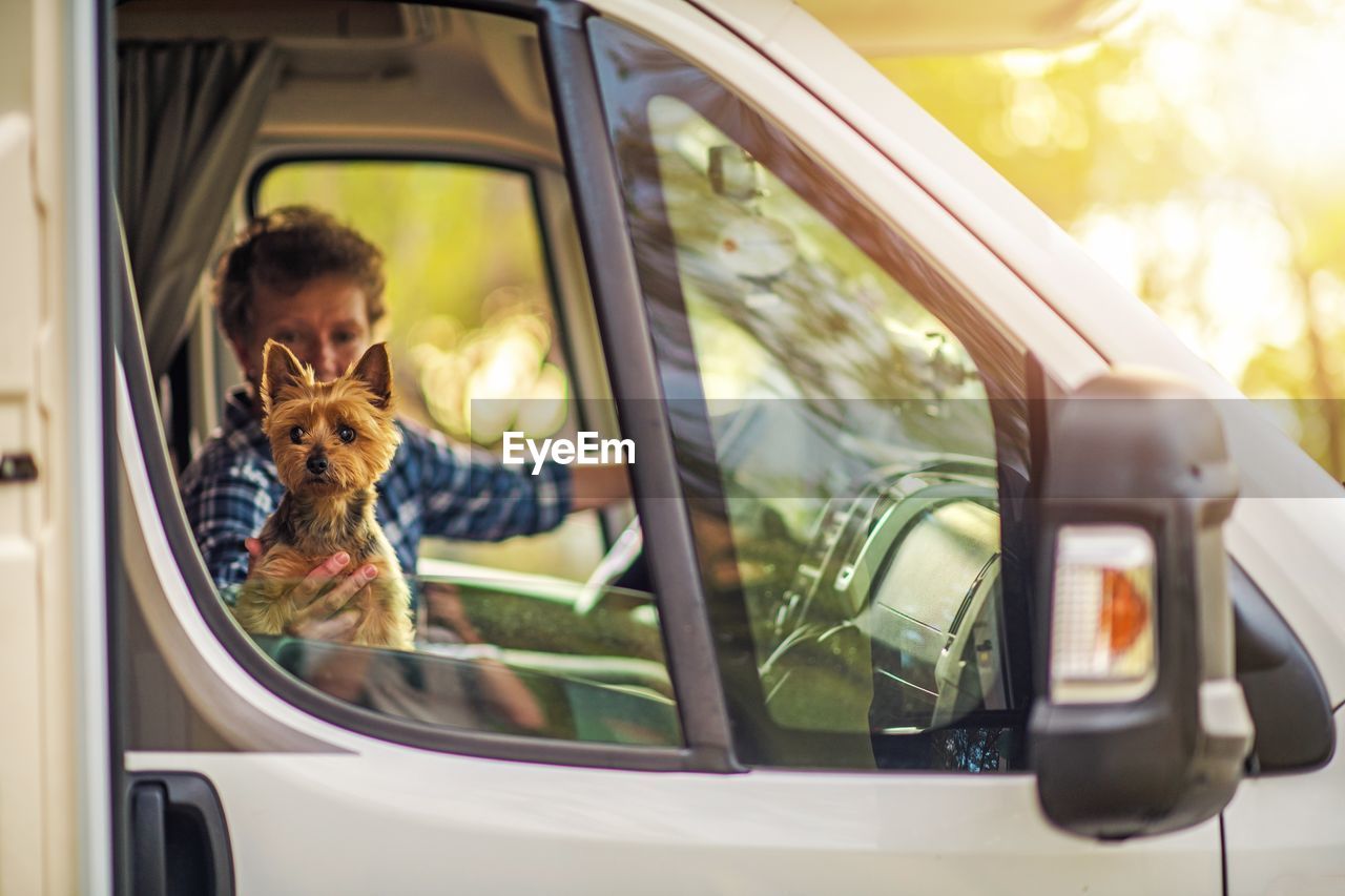 Woman holding dog looking through vehicle window