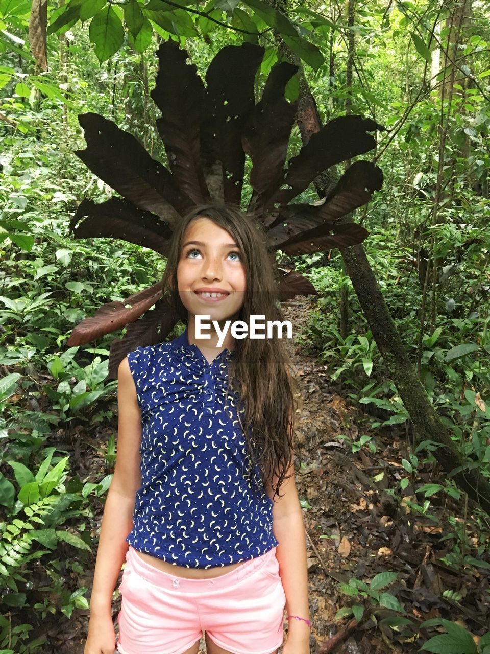 Smiling girl looking up while standing against plants in forest