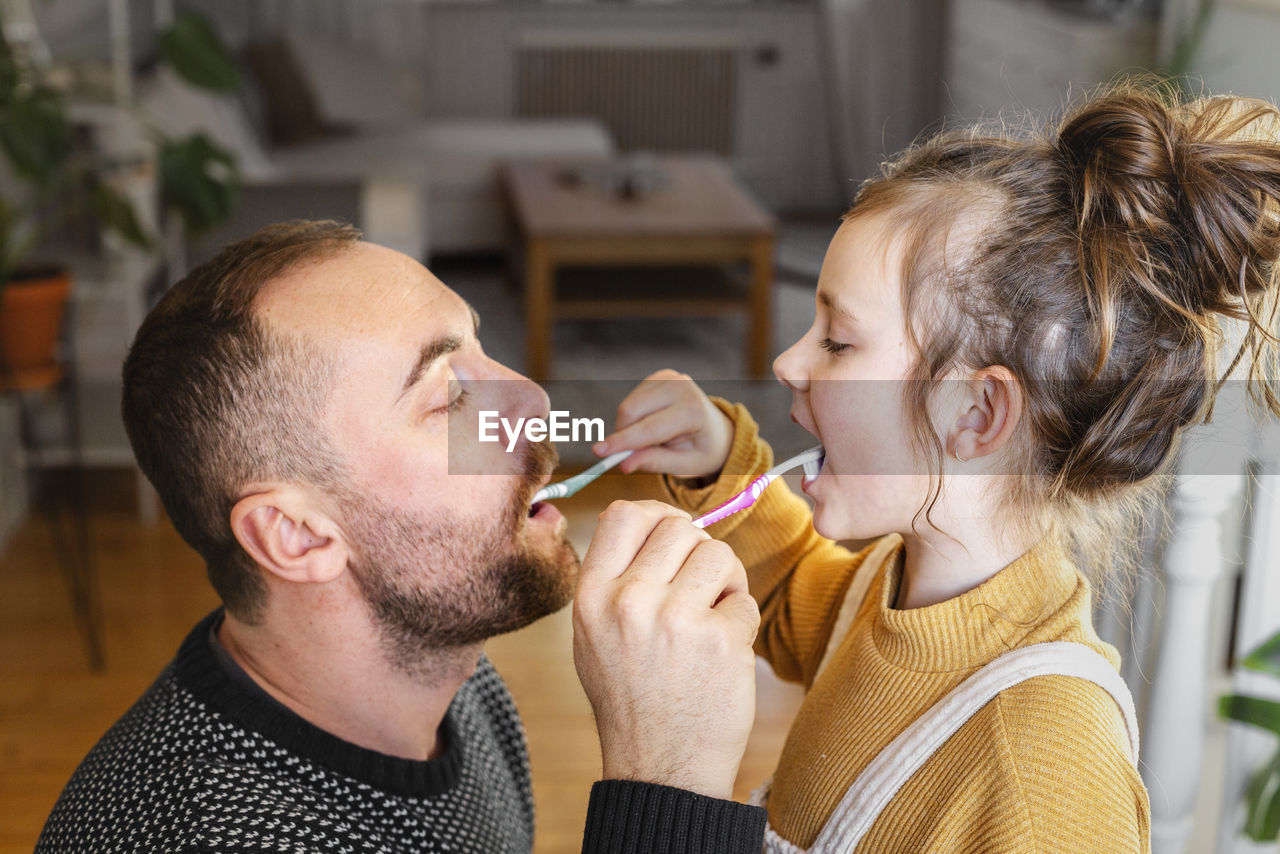 Father and daughter brushing each other teeth