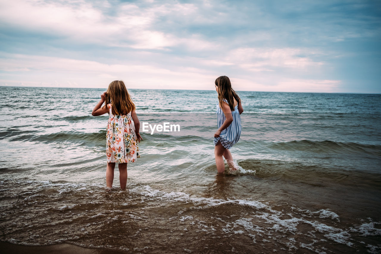 Girls standing in lake in their dresses looking away from camera