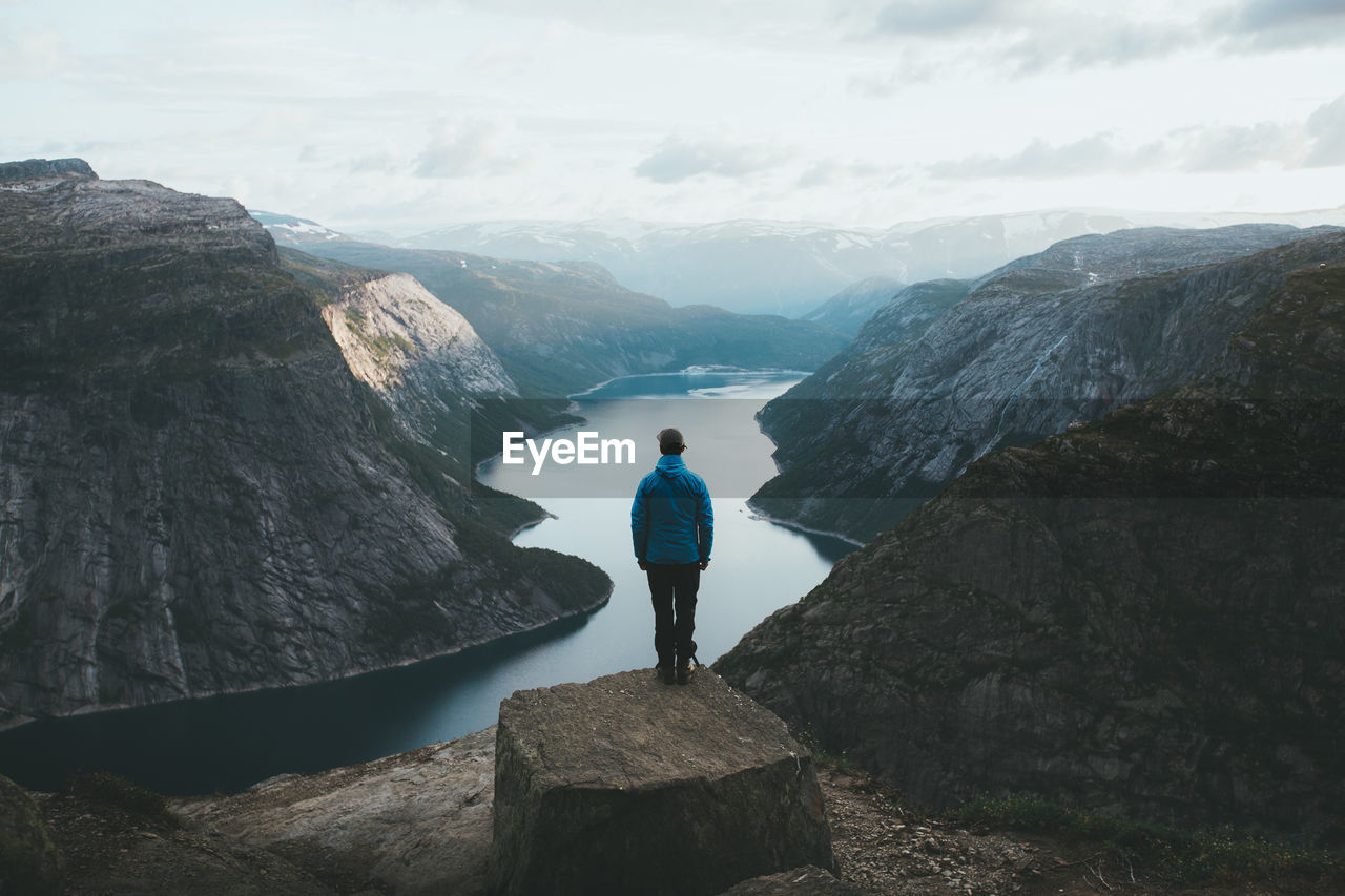 Rear view of man standing on cliff with valley in background against sky