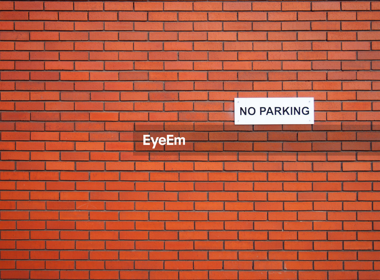 A white sign saying no parking on a red brick wall