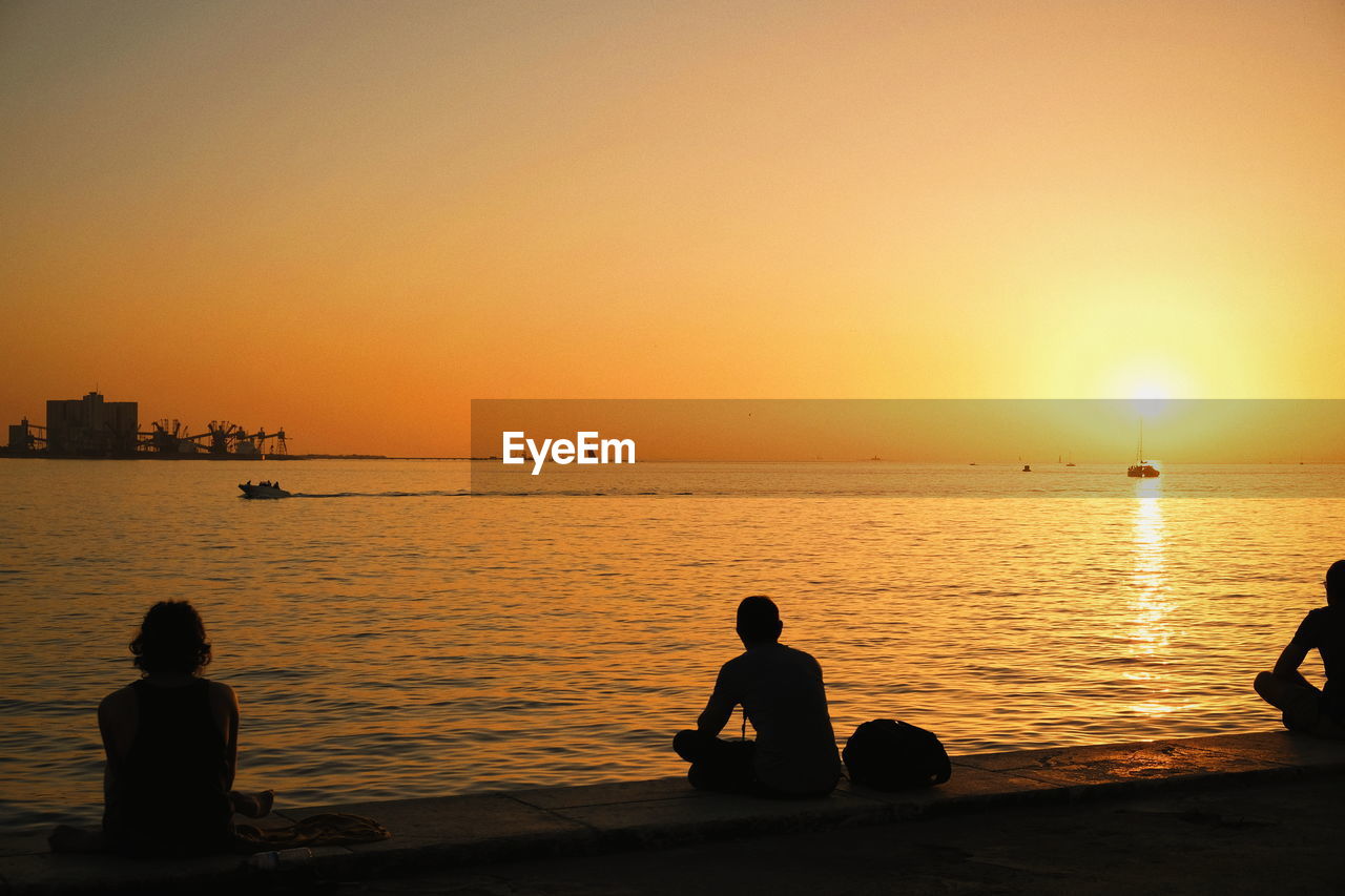 Silhouette people sitting at beach against clear sky during sunset