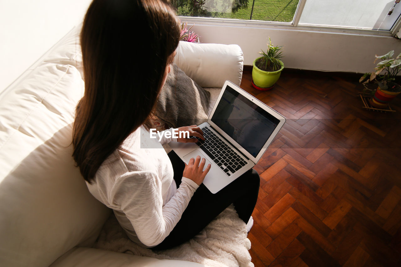 High angle view of woman using laptop while sitting on sofa