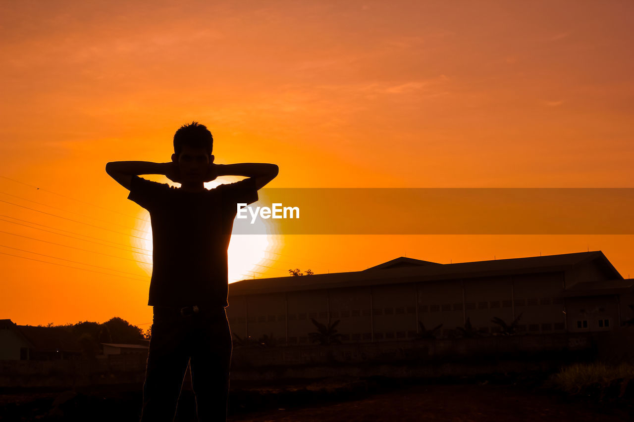 Silhouette man standing on field against orange sky