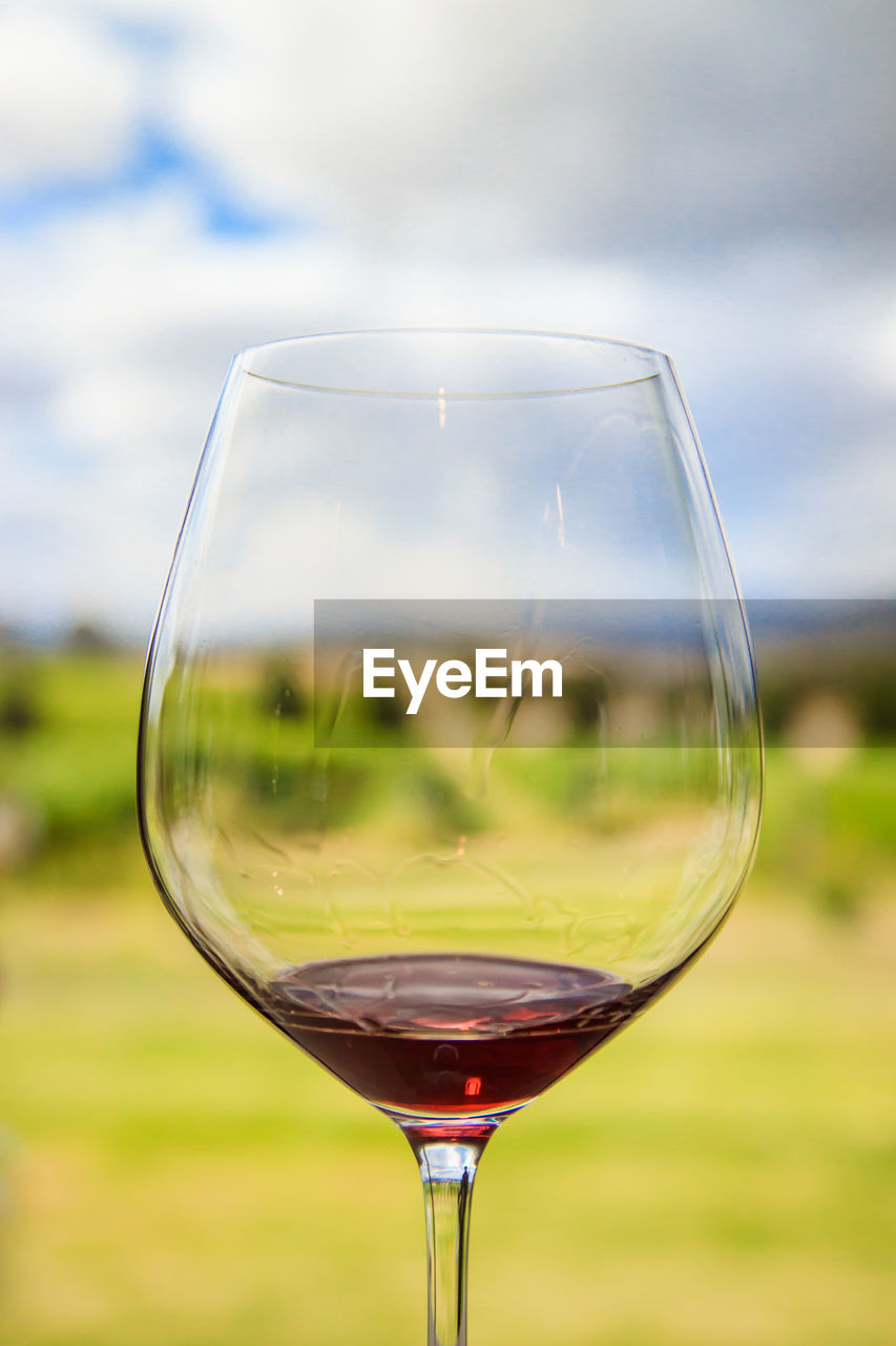 Close-up of red wine in glass on field against sky