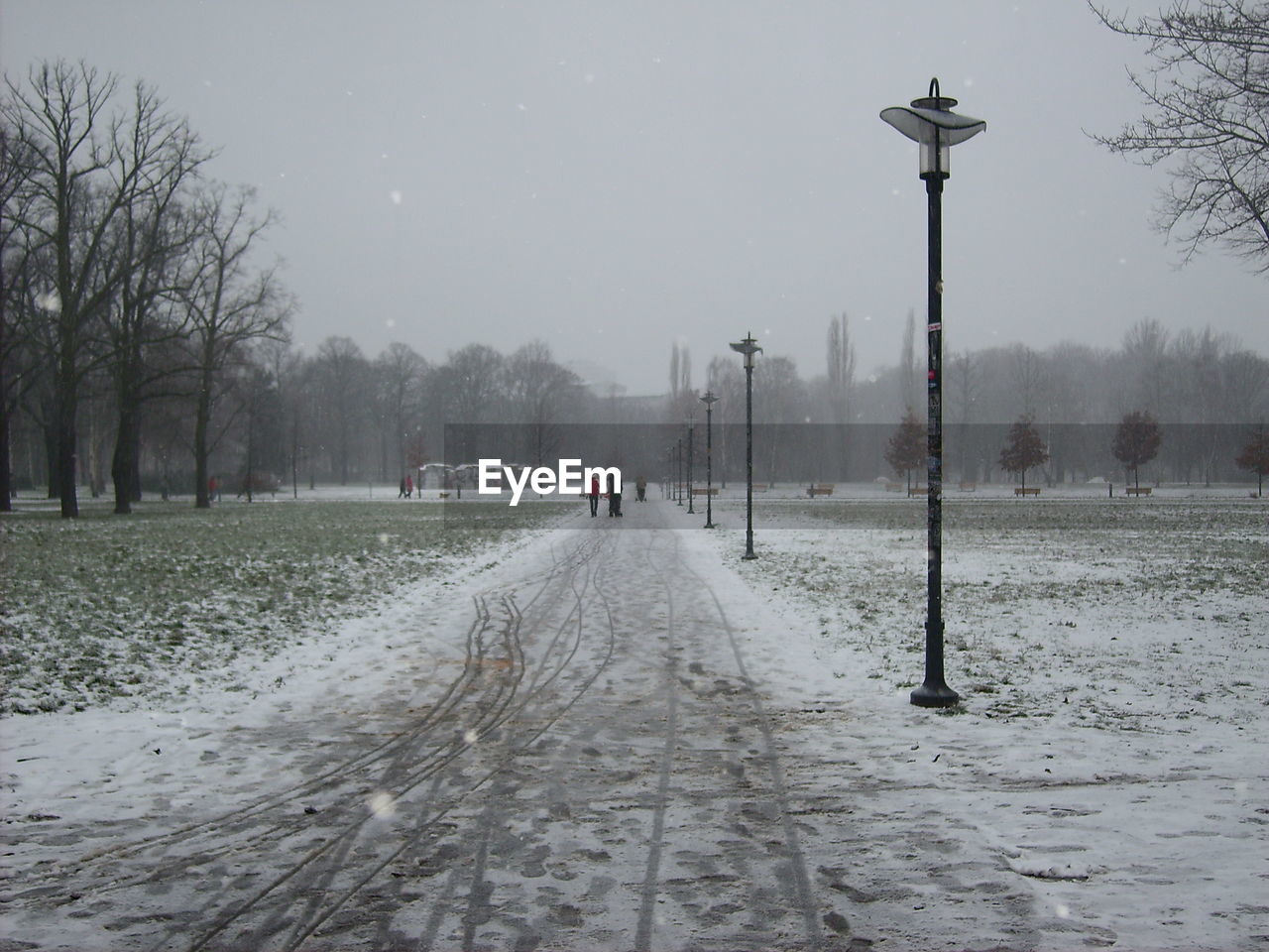 Snow covered field by road against sky