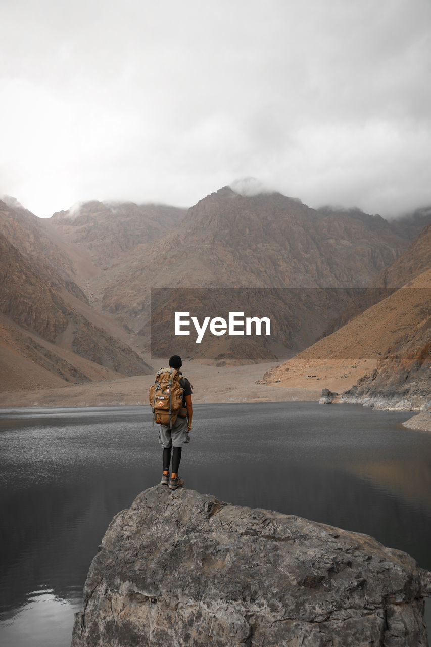 Man standing on rock by mountain against sky