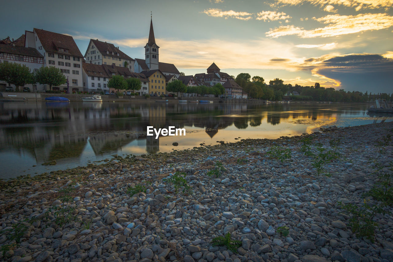 LAKE BY BUILDINGS AGAINST SKY DURING SUNSET