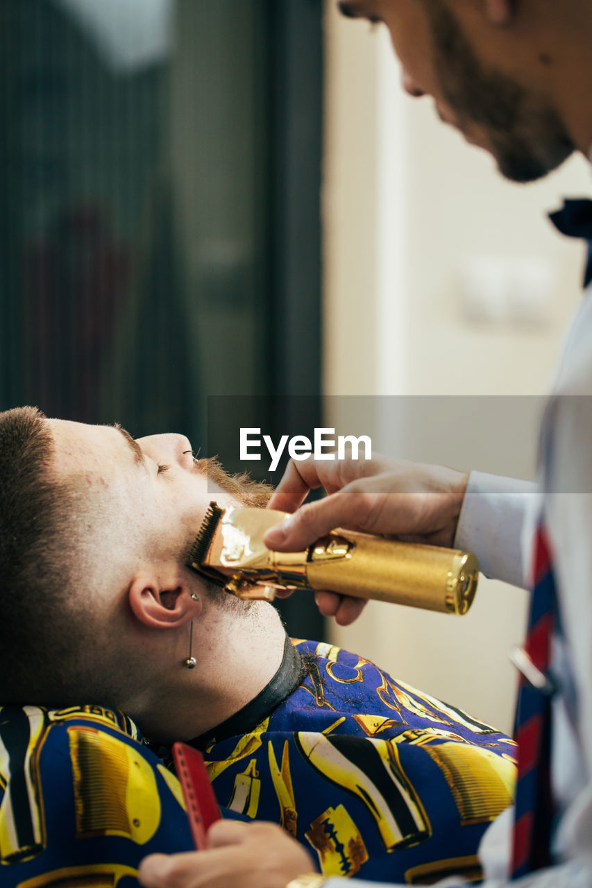 A barber cuts the beard of a man with a clipper in a barbershop