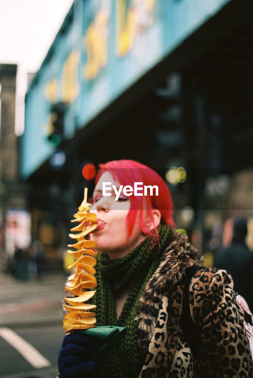 Woman eating from skewer on street in city