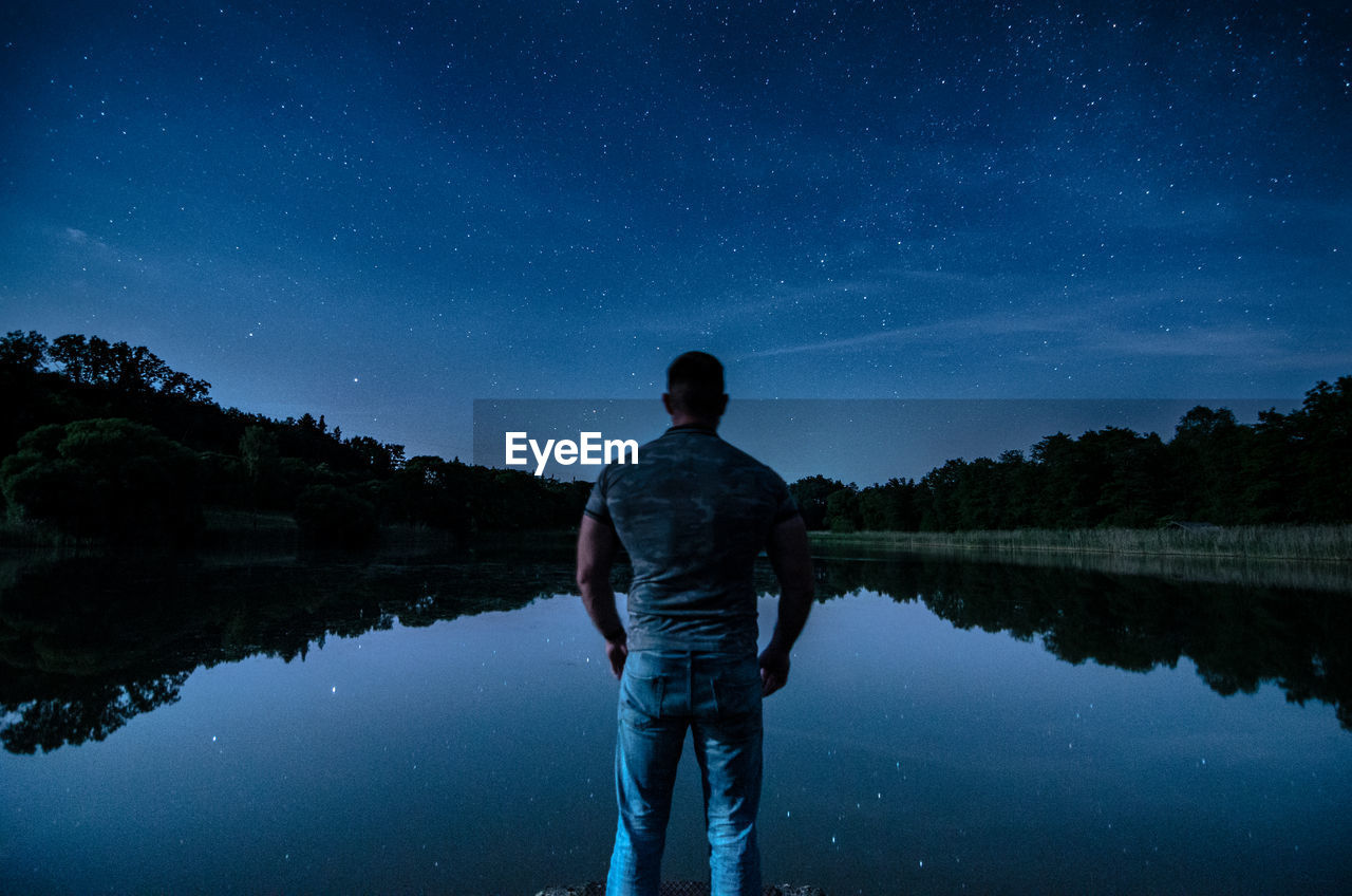 Rear view of man standing in lake against sky at night