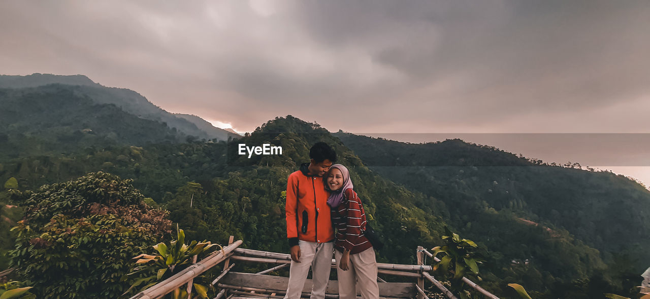 PEOPLE STANDING BY MOUNTAINS AGAINST SKY