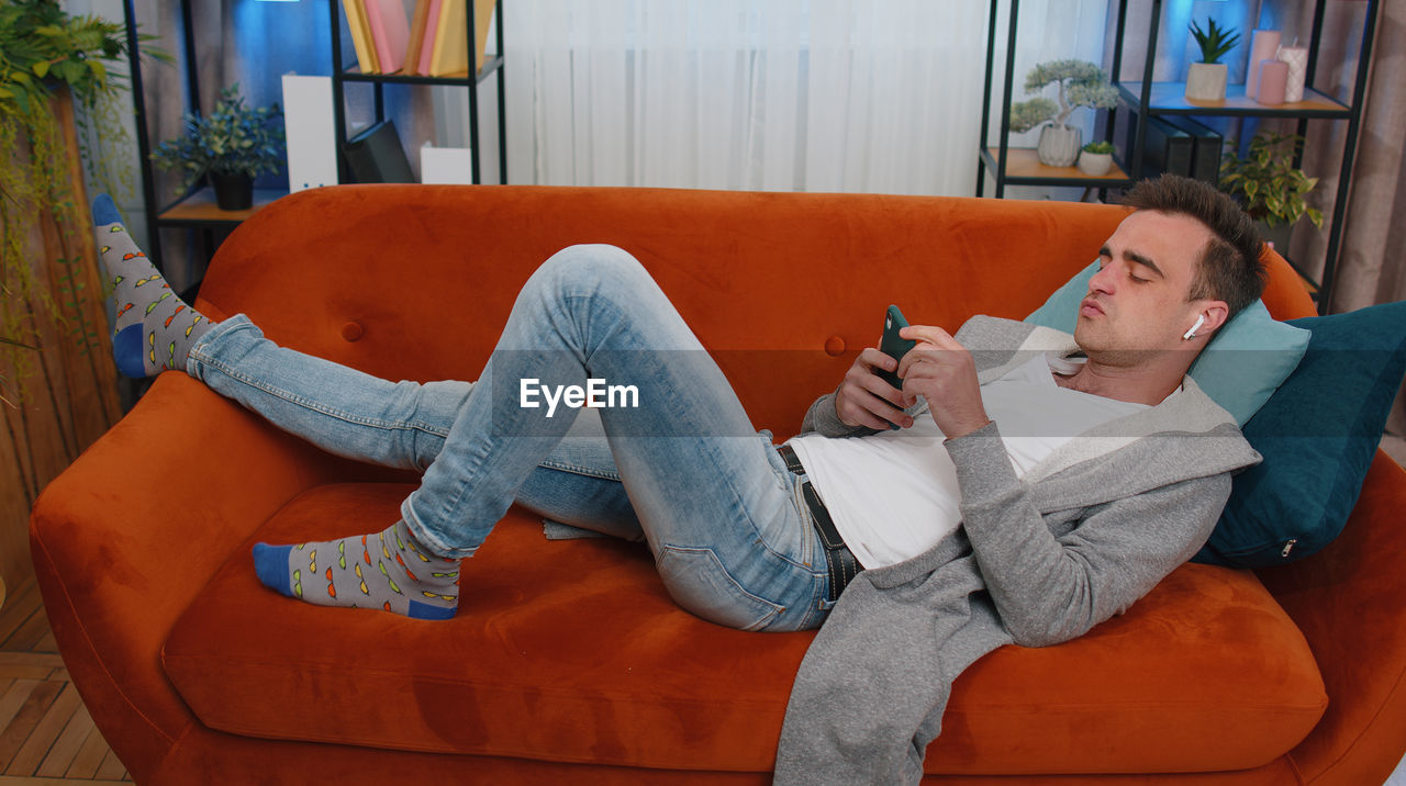 Young man lying on sofa and using smart phone