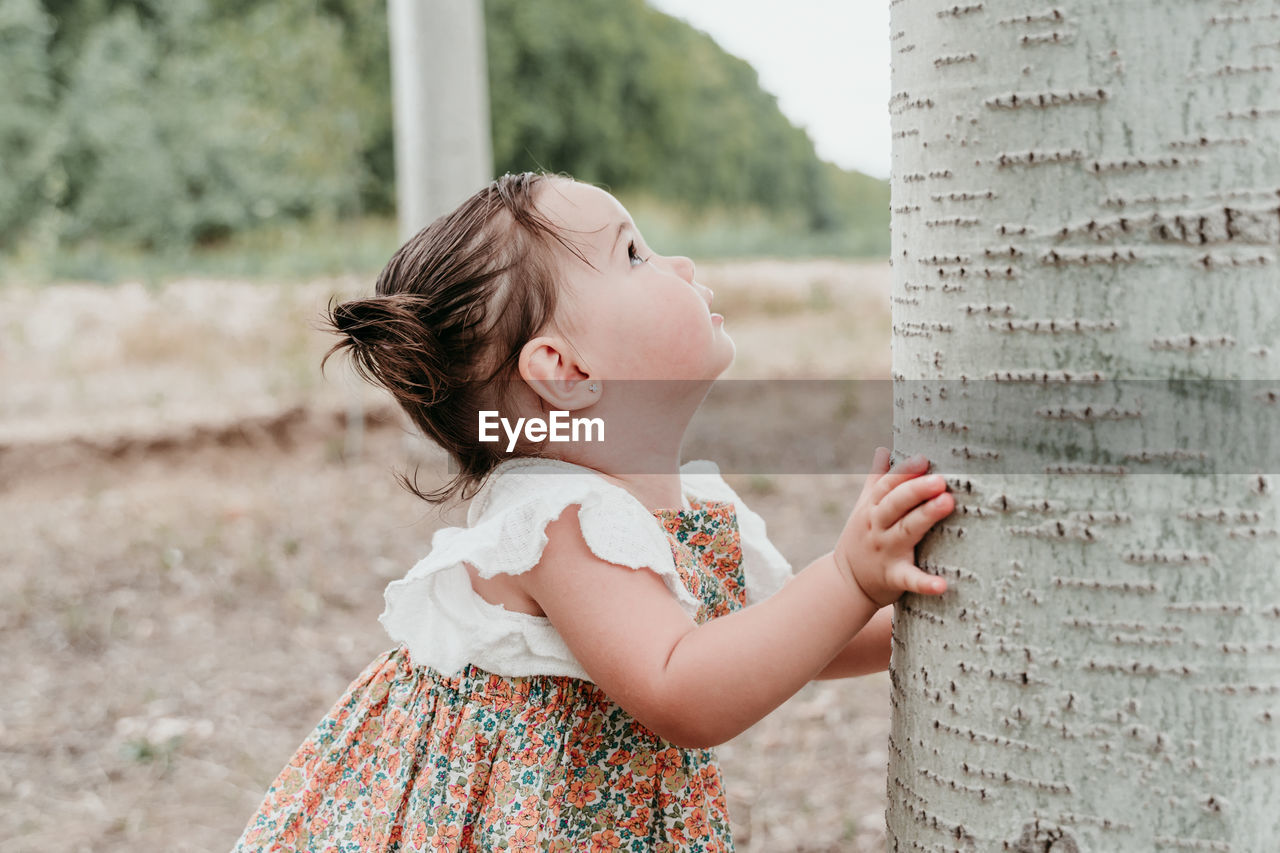 Side view of girl standing by tree