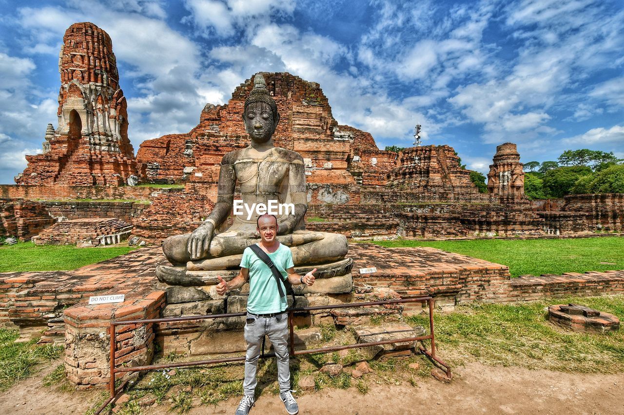 Portrait of man standing against buddha statue