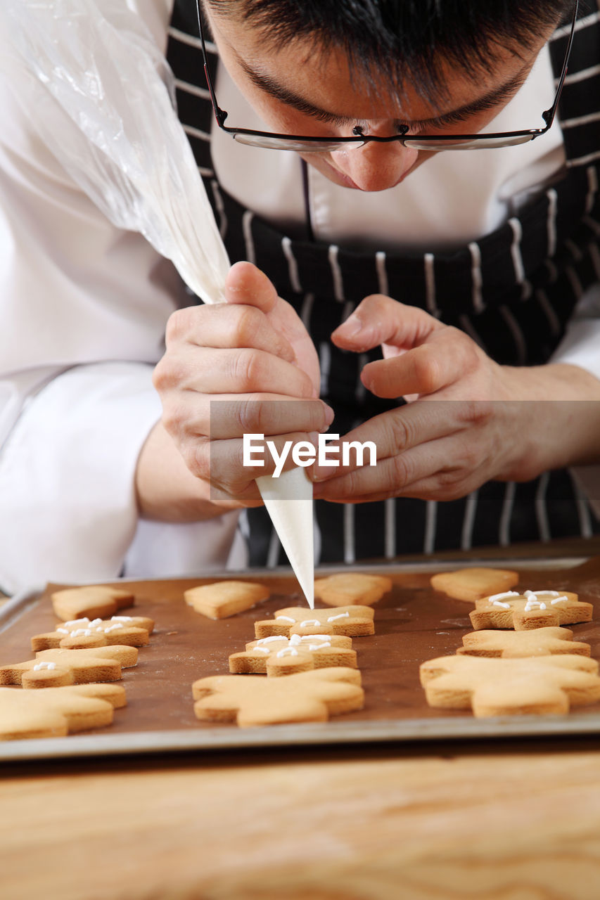 Cropped image of man icing on gingerbread cookies at table