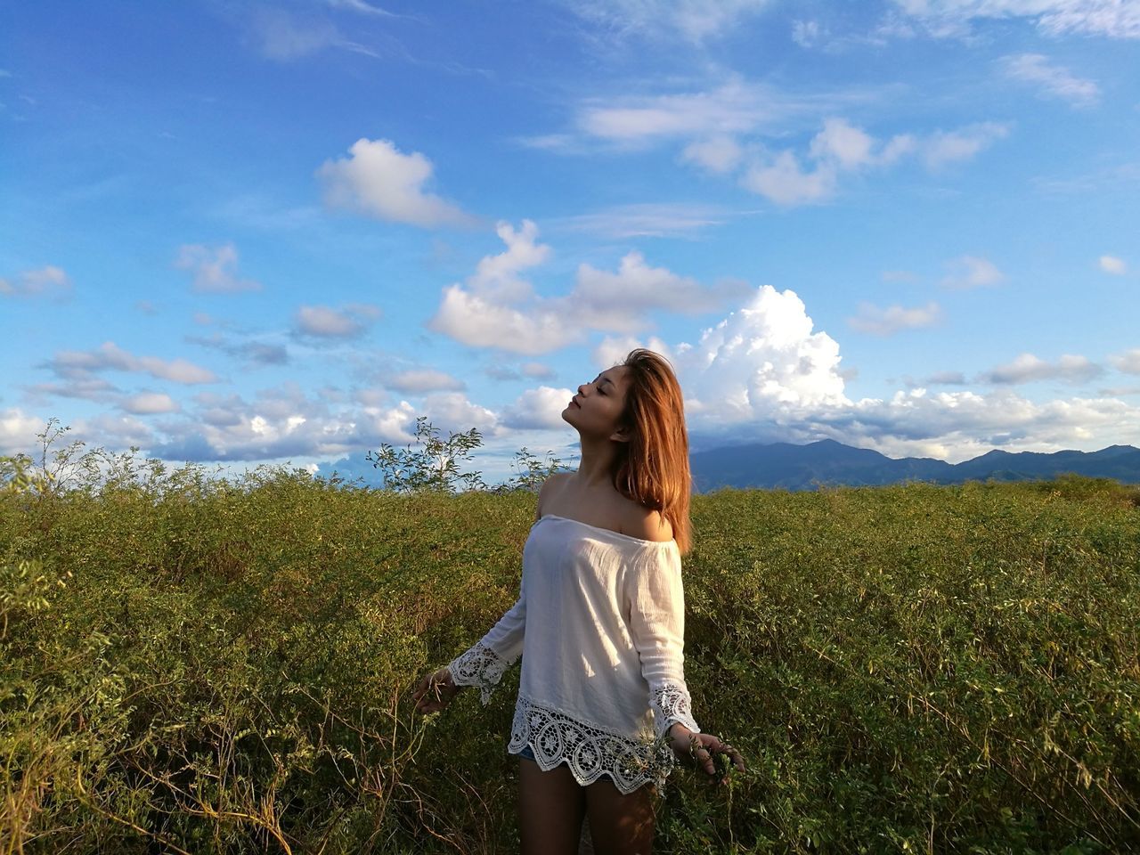 Young woman standing amidst plants against blue sky