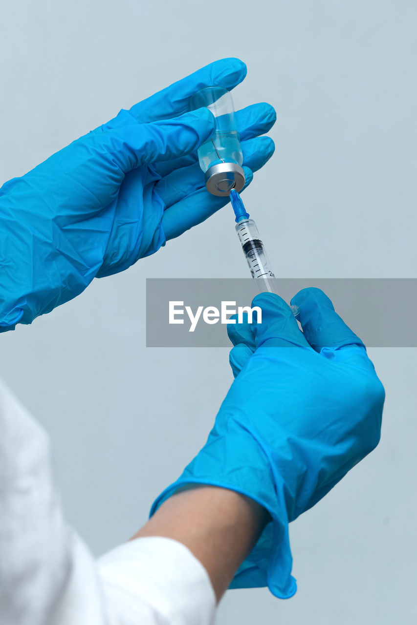 Cropped hands of scientist holding syringe with vial against wall