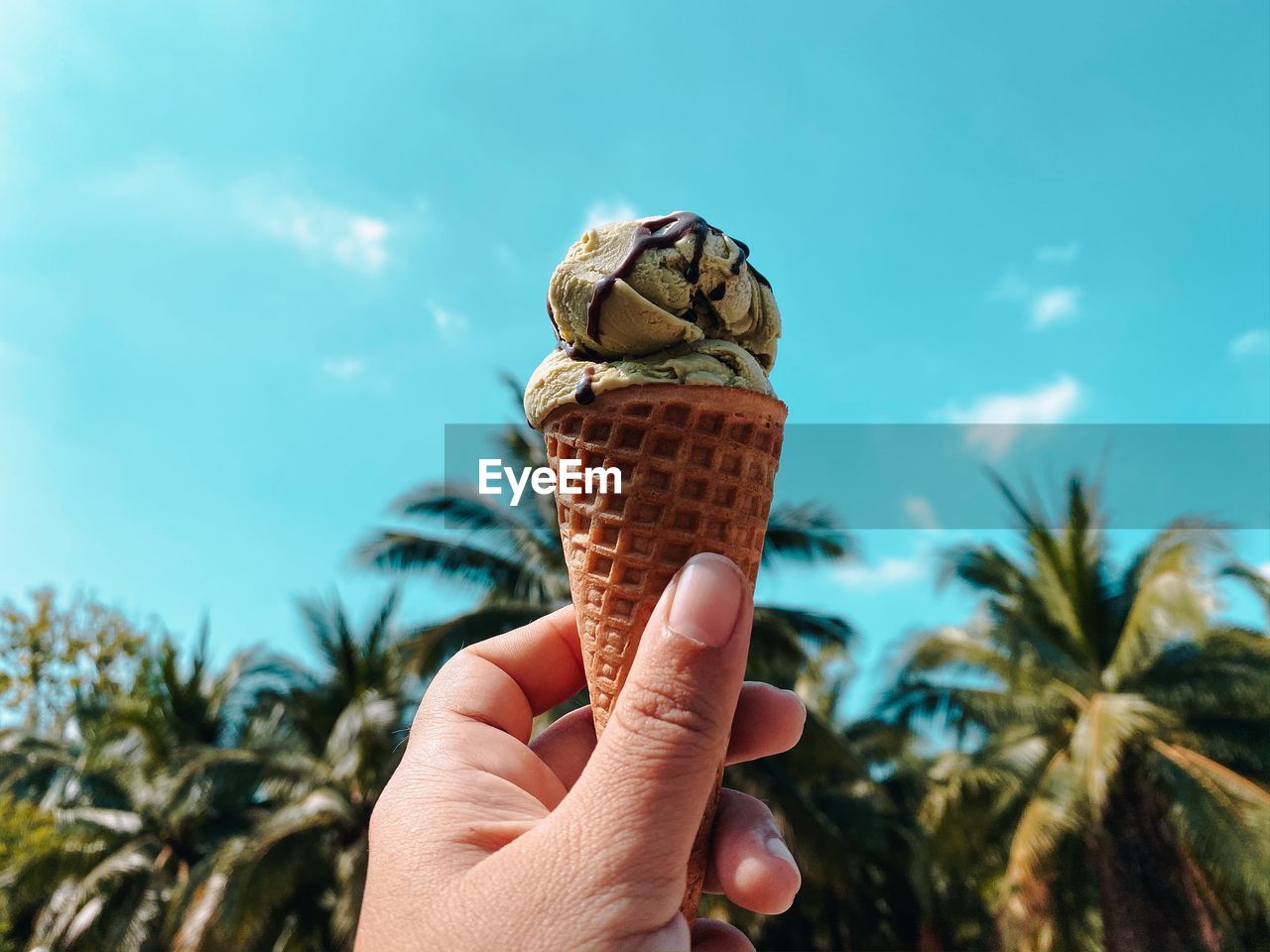 HUMAN HAND HOLDING ICE CREAM CONE AGAINST SKY