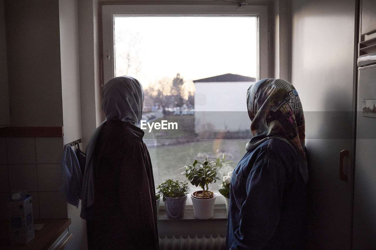 Thoughtful women in headscarves looking through window