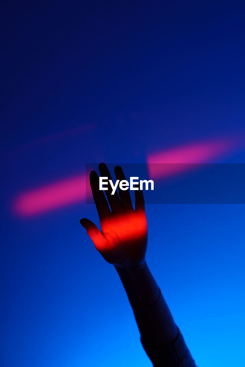 Woman arm gesturing with open hand over fashion blue background, neon red light on wrist and wall