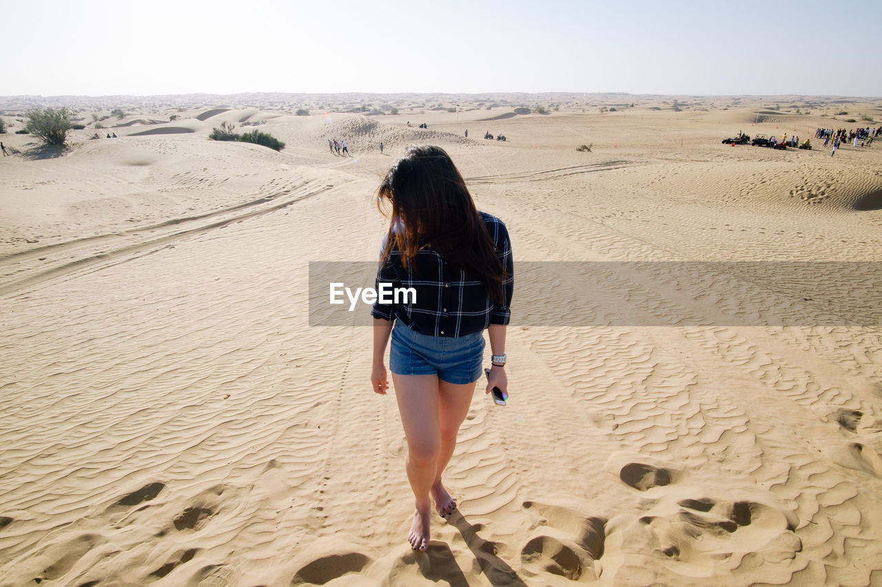 Woman walking on sand dune hill during sunny day