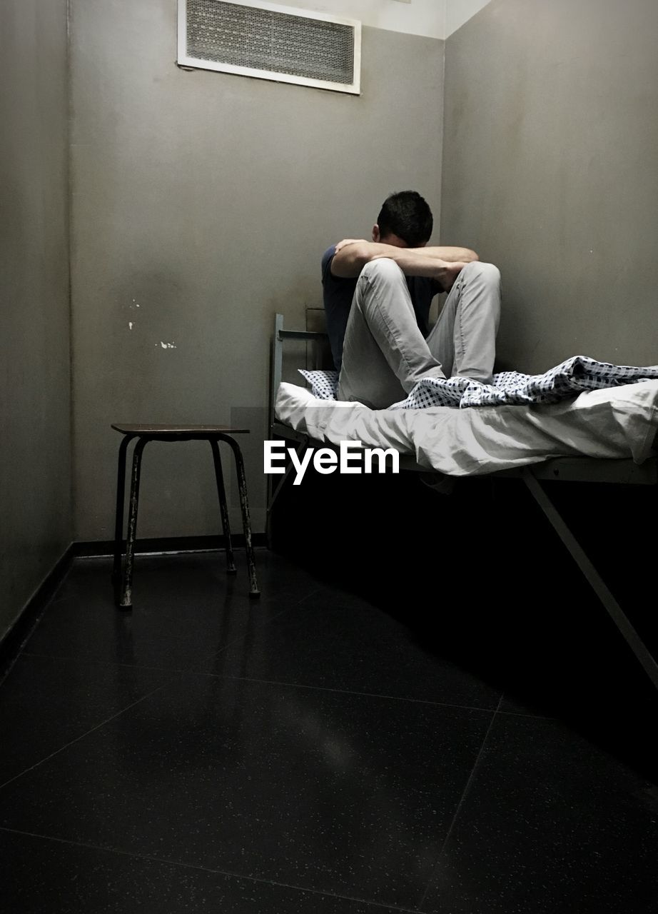 Male prisoner sitting on bed in prison