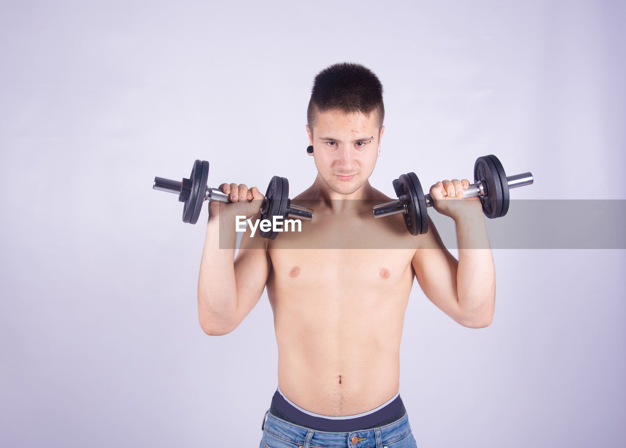 Shirtless man lifting dumbbells against purple background