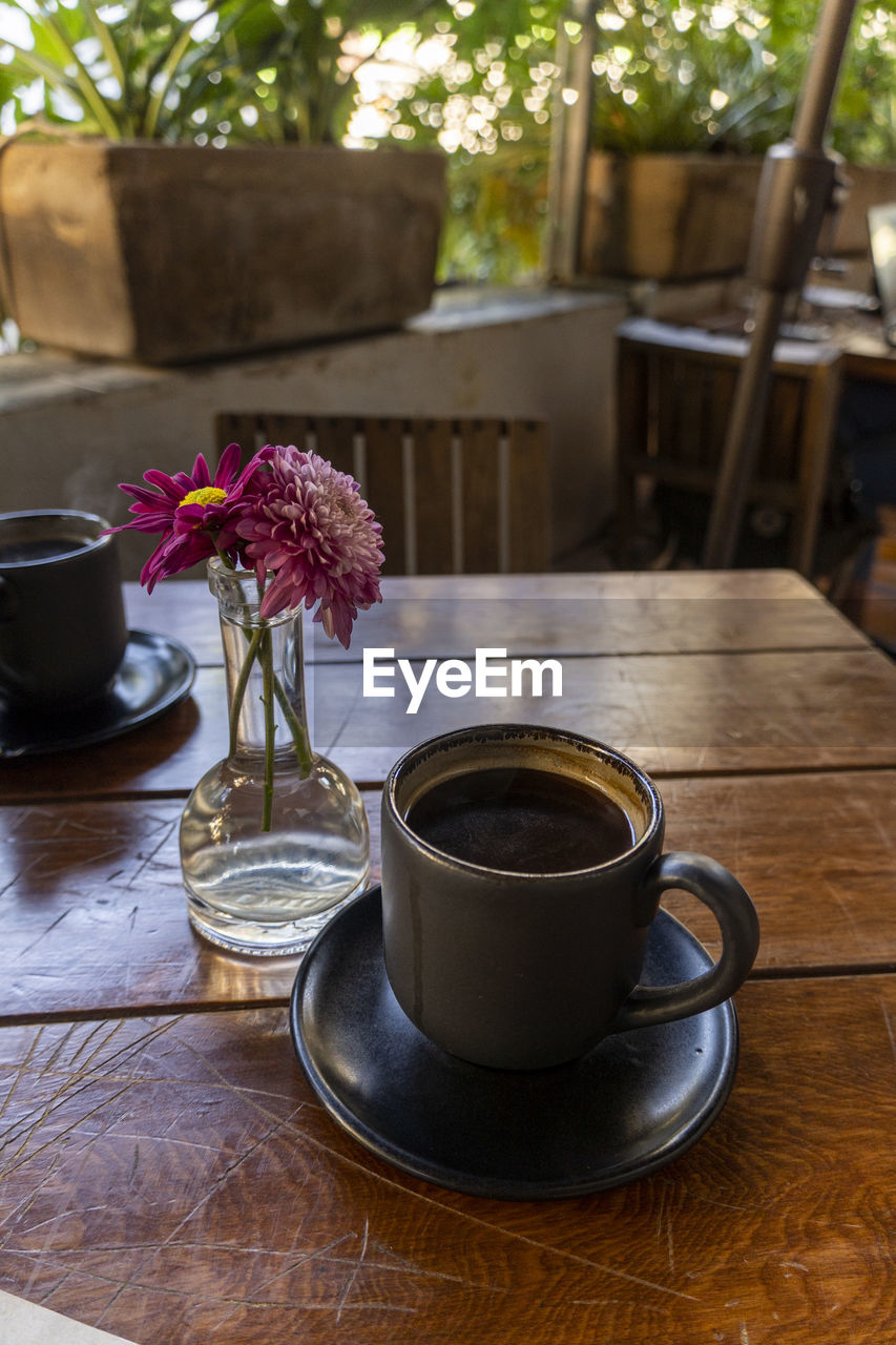 mug, drink, cup, food and drink, coffee cup, coffee, table, refreshment, crockery, hot drink, flowering plant, saucer, flower, wood, tea, freshness, plant, tableware, nature, serveware, no people, indoors, food, kitchen utensil, still life, furniture, spoon, day, tea cup, turkish coffee, cafe, household equipment, coffeehouse, seat, vase, lifestyles, chair, eating utensil, window