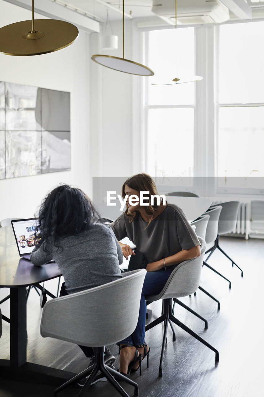 Female colleagues discussing over laptop computer in conference room at creative office