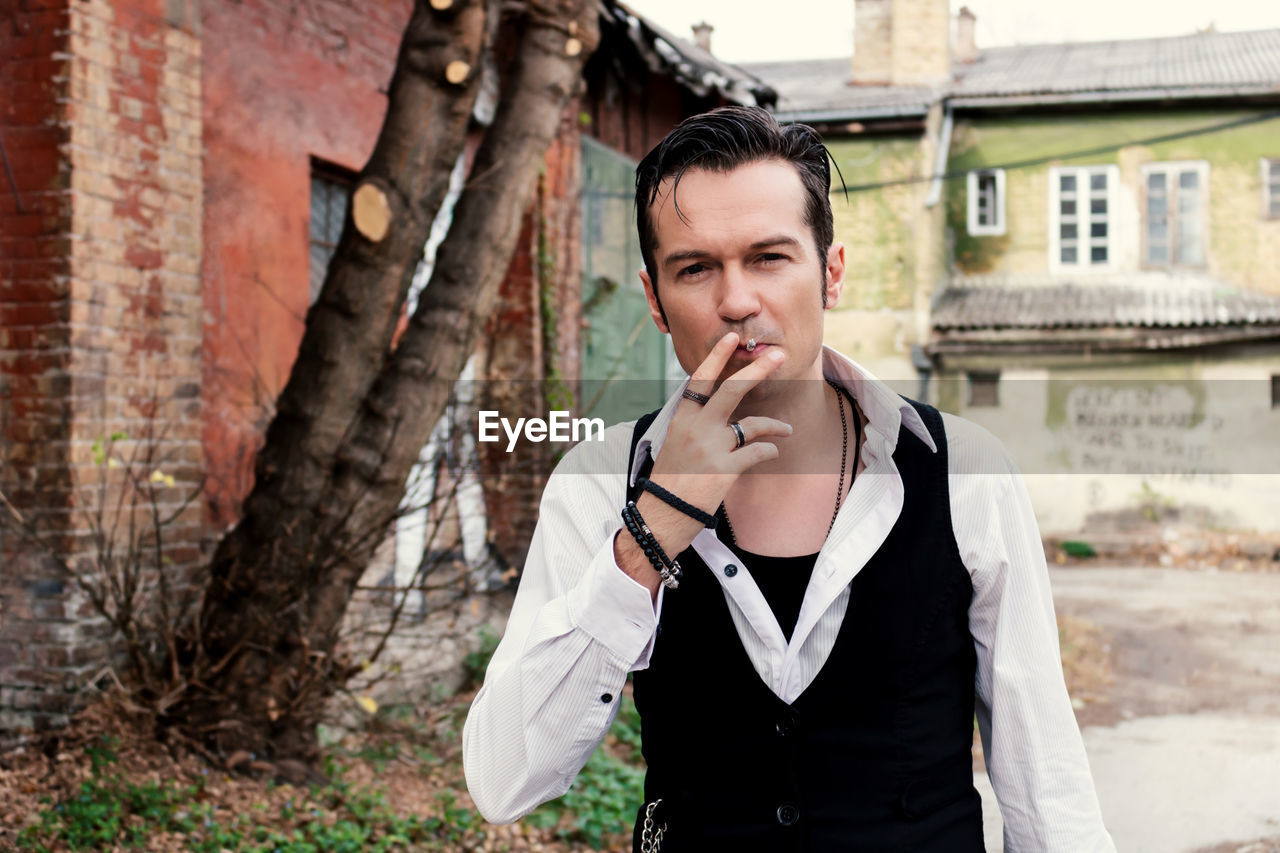 Self-confident retro-styled man smoking cigarette outdoors and looking at camera.